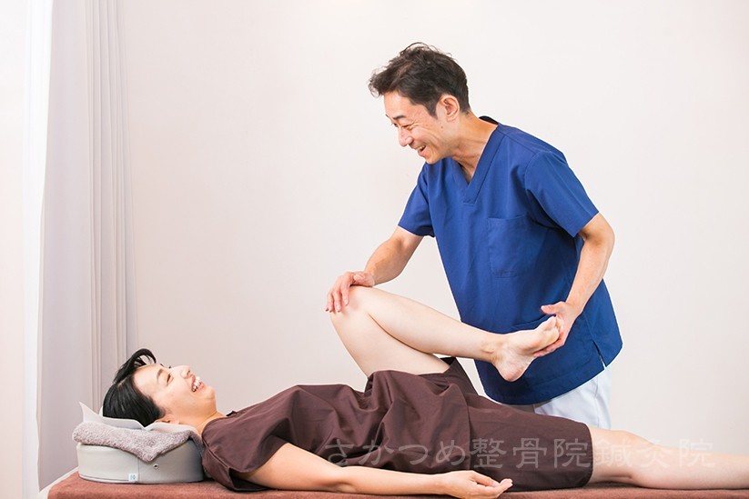 あお向けの人の脚を持ち上げる施術者