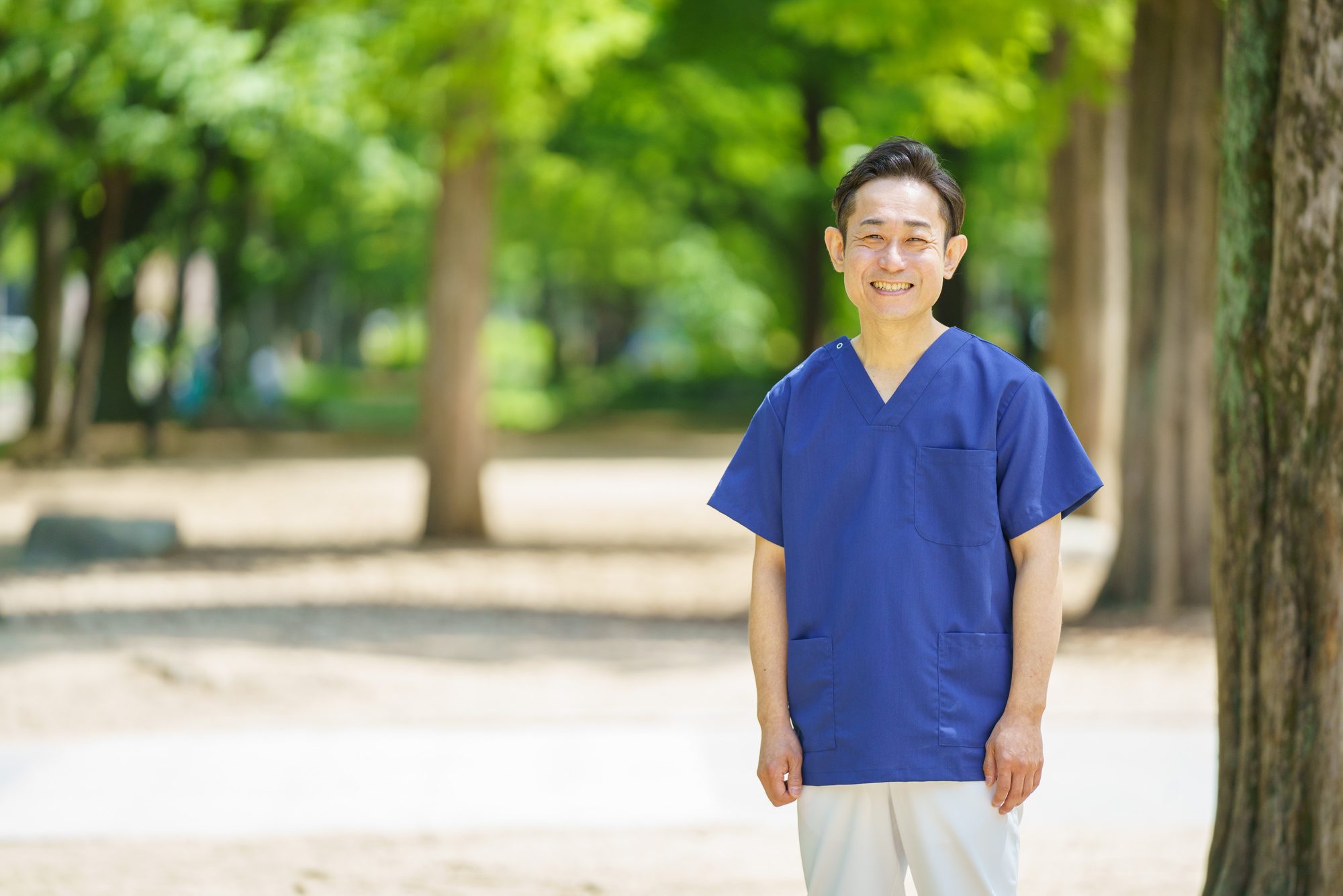木立を背に立つ施術着姿の施術者